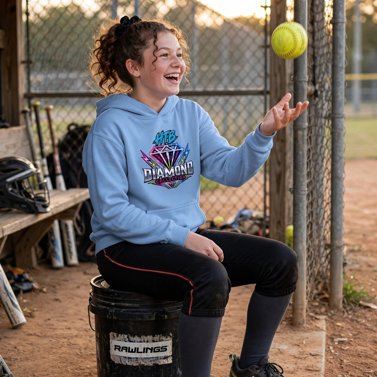 HTB Diamond Collection Youth Hoodie in Carolina Blue — girl softball player flipping a softball on a ball bucket