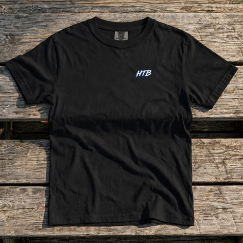 HTB Youth Do Damage Heavyweight Tee in Black - front flat lay on a dugout bench